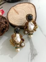 A glamorous set of earrings featuring irregular baroque pearls, large gemstone studs, and floral gold accents with crystal embellishments, displayed on a marble surface with wooden slices for contrast.
