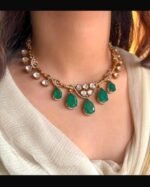 A traditional gold-tone kundan necklace with teardrop-shaped green emerald stones and shimmering white kundan detailing, worn with an ivory outfit.