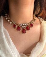 A traditional gold-tone kundan necklace with teardrop-shaped green emerald stones and shimmering white kundan detailing, worn with an ivory outfit.