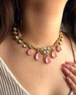 A traditional gold-tone kundan necklace with teardrop-shaped green emerald stones and shimmering white kundan detailing, worn with an ivory outfit.