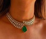 A crescent-shaped gold kundan choker adorned with white teardrop stones and a single green emerald pendant hanging in the center, worn on a bare neckline.