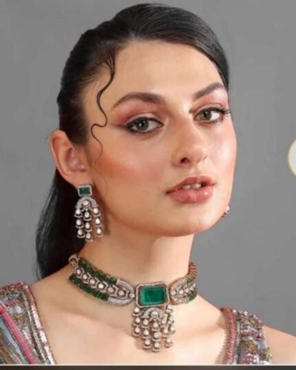 A woman wearing a green and silver kundan choker with a square emerald centerpiece and matching jhumka earrings, styled with a traditional outfit.