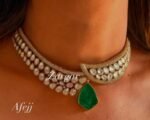 A crescent-shaped gold kundan choker adorned with white teardrop stones and a single green emerald pendant hanging in the center, worn on a bare neckline.