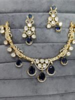 A traditional gold-tone kundan necklace with teardrop-shaped green emerald stones and shimmering white kundan detailing, worn with an ivory outfit.