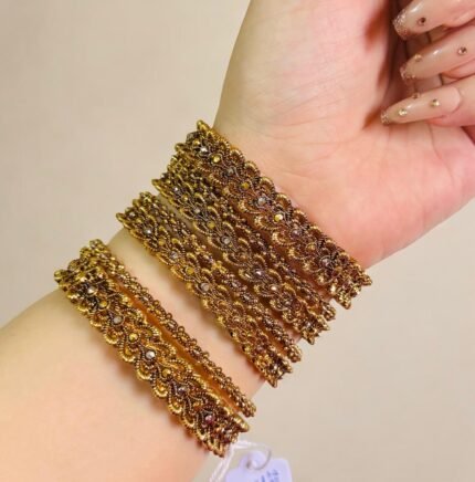 Traditional gold-plated bangles set with intricate detailing, elegantly worn on a woman’s wrist for a festive or cultural occasion