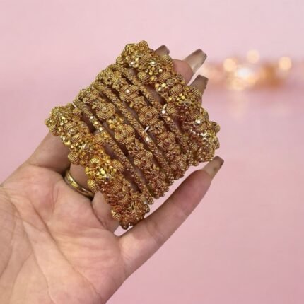Hand wearing a set of gold-plated crystal bangles with intricate detailing