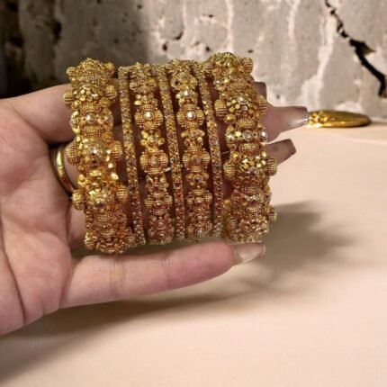 Hand wearing a set of gold-plated crystal bangles with intricate detailing