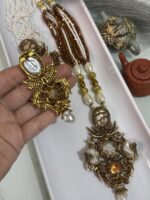 Three ornate antique-style necklaces with multistrand pearl and brown beads, featuring large gold-toned pendants embellished with pearls, gemstones, and intricate carved designs, displayed on a white tray.