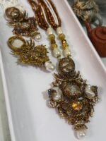 Three ornate antique-style necklaces with multistrand pearl and brown beads, featuring large gold-toned pendants embellished with pearls, gemstones, and intricate carved designs, displayed on a white tray.