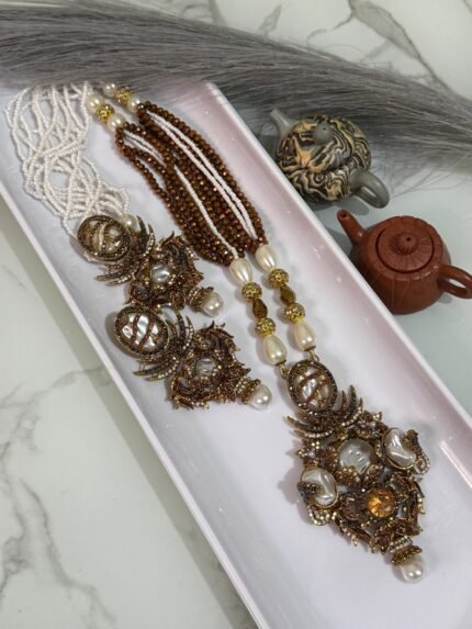 Three ornate antique-style necklaces with multistrand pearl and brown beads, featuring large gold-toned pendants embellished with pearls, gemstones, and intricate carved designs, displayed on a white tray.