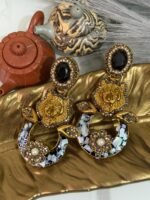 A pair of bold statement earrings with green gemstone studs, gold tiger heads, leaf accents, and circular bases decorated with iridescent shell inlay and floral designs.