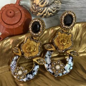 A pair of bold statement earrings with green gemstone studs, gold tiger heads, leaf accents, and circular bases decorated with iridescent shell inlay and floral designs.