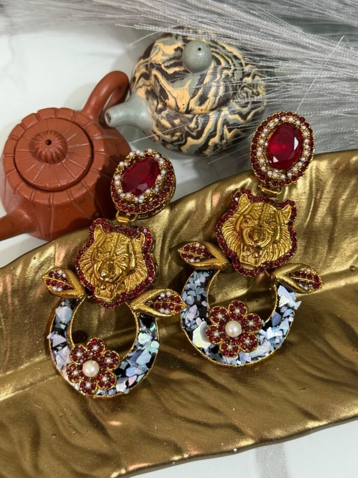 A pair of bold statement earrings with green gemstone studs, gold tiger heads, leaf accents, and circular bases decorated with iridescent shell inlay and floral designs.