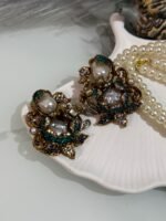 Pearl choker necklace with green and white kundan earrings displayed on a shell tray with decorative props.
