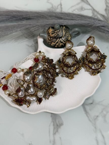 Kundan choker set with red and white beads, large pearl drops, and matching earrings displayed on a shell tray.