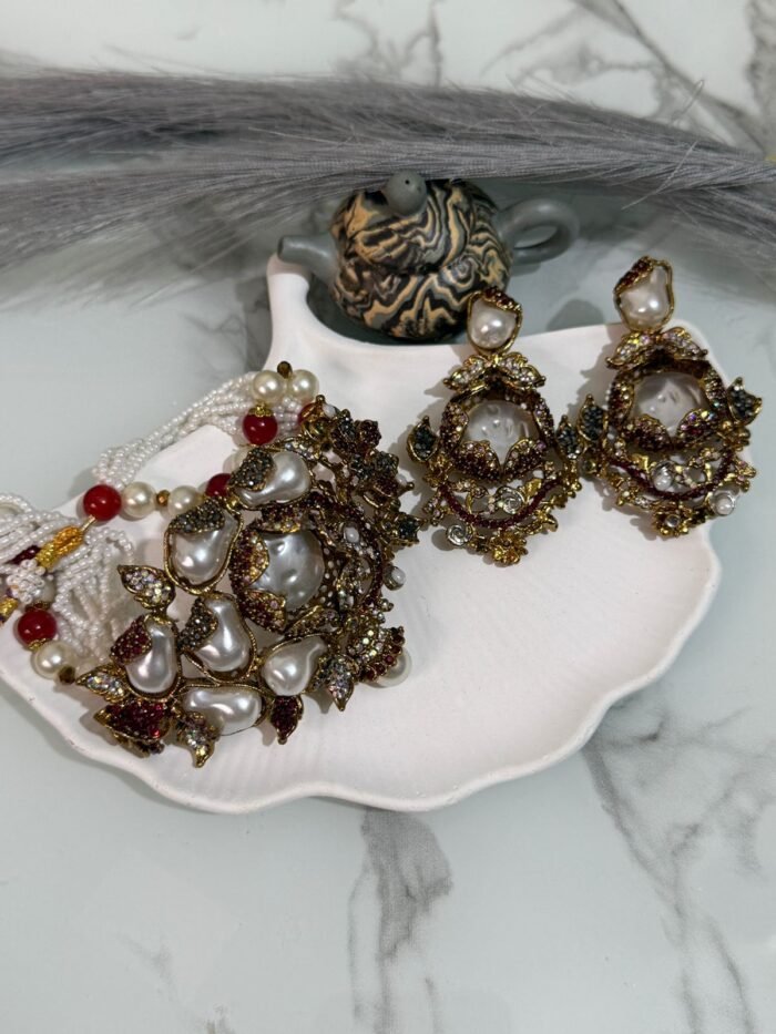 Kundan choker set with red and white beads, large pearl drops, and matching earrings displayed on a shell tray.