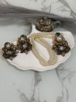 Pearl choker necklace with green and white kundan earrings displayed on a shell tray with decorative props.