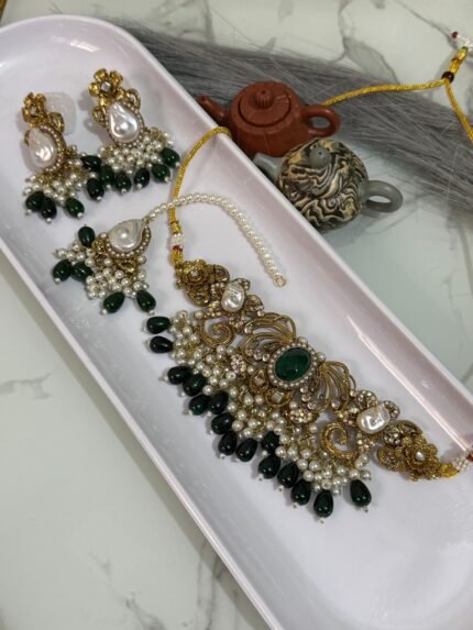 Traditional bridal choker jewelry set with green beads, pearl drops, and matching earrings and maang tikka displayed in a white tray.