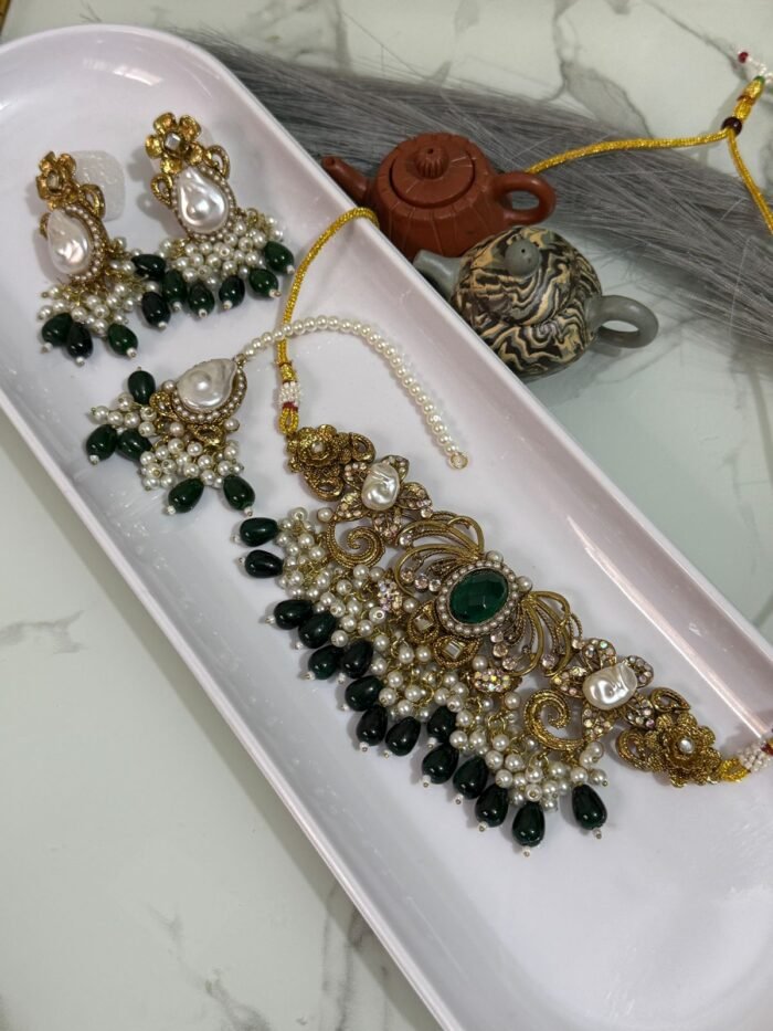 Traditional bridal choker jewelry set with green beads, pearl drops, and matching earrings and maang tikka displayed in a white tray.