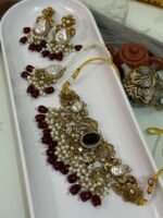 Traditional gold choker jewelry set with black center stone, maroon bead drops, pearls, and matching earrings and maang tikka, displayed in a white tray.