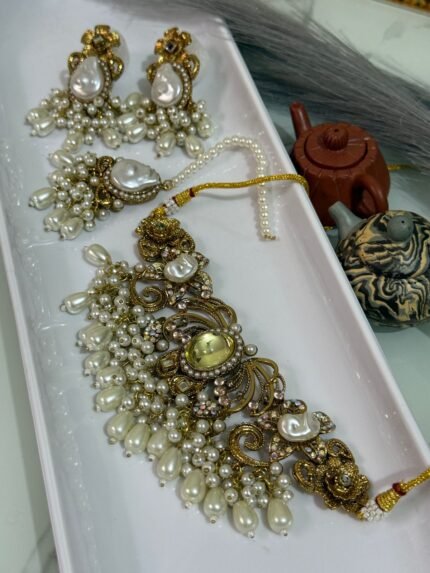 Gold choker jewelry set with yellow center stone, cream pearl drops, and matching earrings and maang tikka displayed in a white tray.