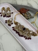 Traditional gold choker jewelry set with black center stone, maroon bead drops, pearls, and matching earrings and maang tikka, displayed in a white tray.