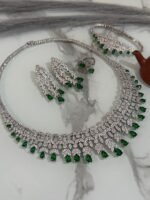 Emerald and diamond necklace set with matching bracelet, earrings, and ring displayed on a marble surface.