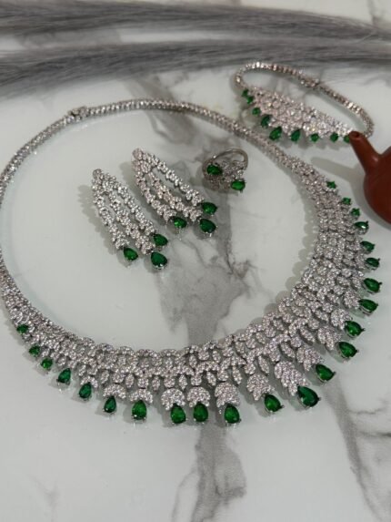 Emerald and diamond necklace set with matching bracelet, earrings, and ring displayed on a marble surface.