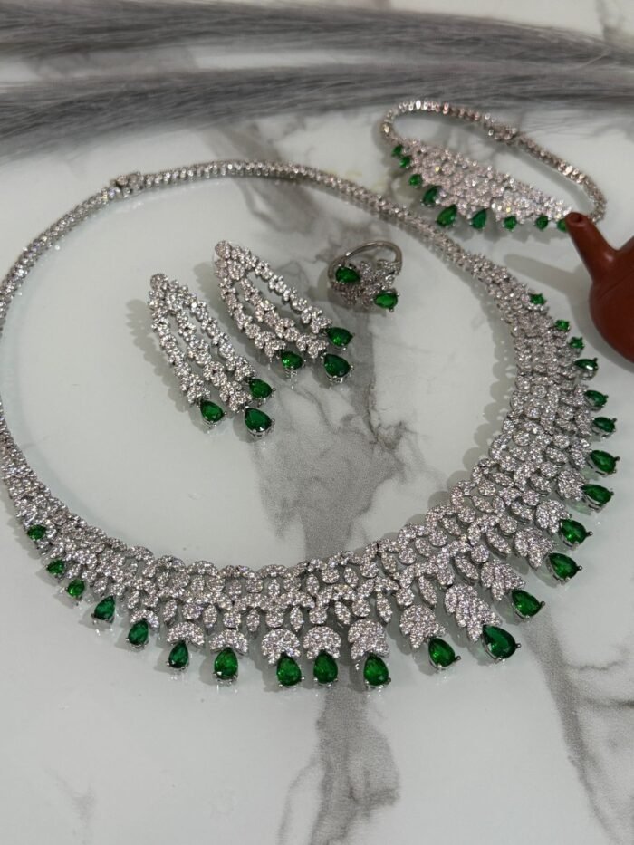 Emerald and diamond necklace set with matching bracelet, earrings, and ring displayed on a marble surface.