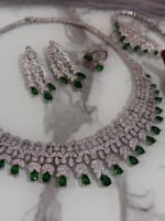 Emerald and diamond necklace set with matching bracelet, earrings, and ring displayed on a marble surface.