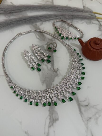 Emerald and diamond necklace set with matching bracelet, earrings, and ring displayed on a marble surface.