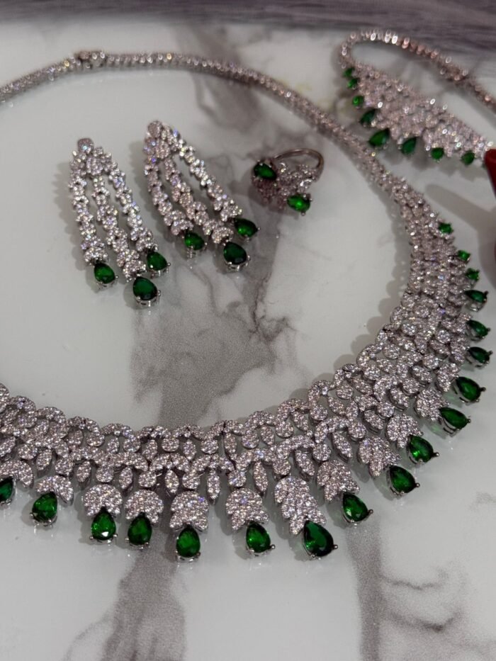 Emerald and diamond necklace set with matching bracelet, earrings, and ring displayed on a marble surface.