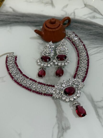Ruby and diamond necklace set with matching earrings displayed on a marble surface, featuring a rich ruby strand and sparkling diamonds.
