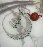 Emerald and diamond necklace set with matching bracelet, earrings, and ring displayed on a marble surface.