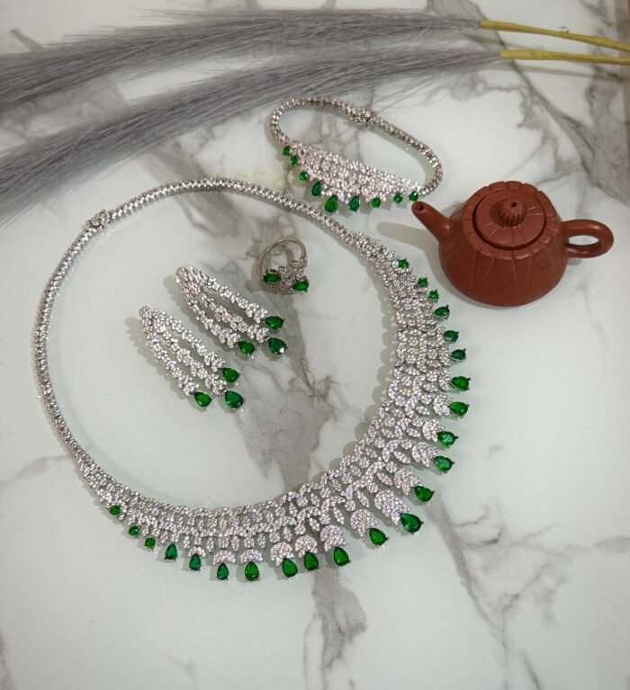 Emerald and diamond necklace set with matching bracelet, earrings, and ring displayed on a marble surface.