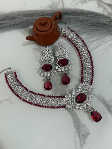 Ruby and diamond necklace set with matching earrings displayed on a marble surface, featuring a rich ruby strand and sparkling diamonds.