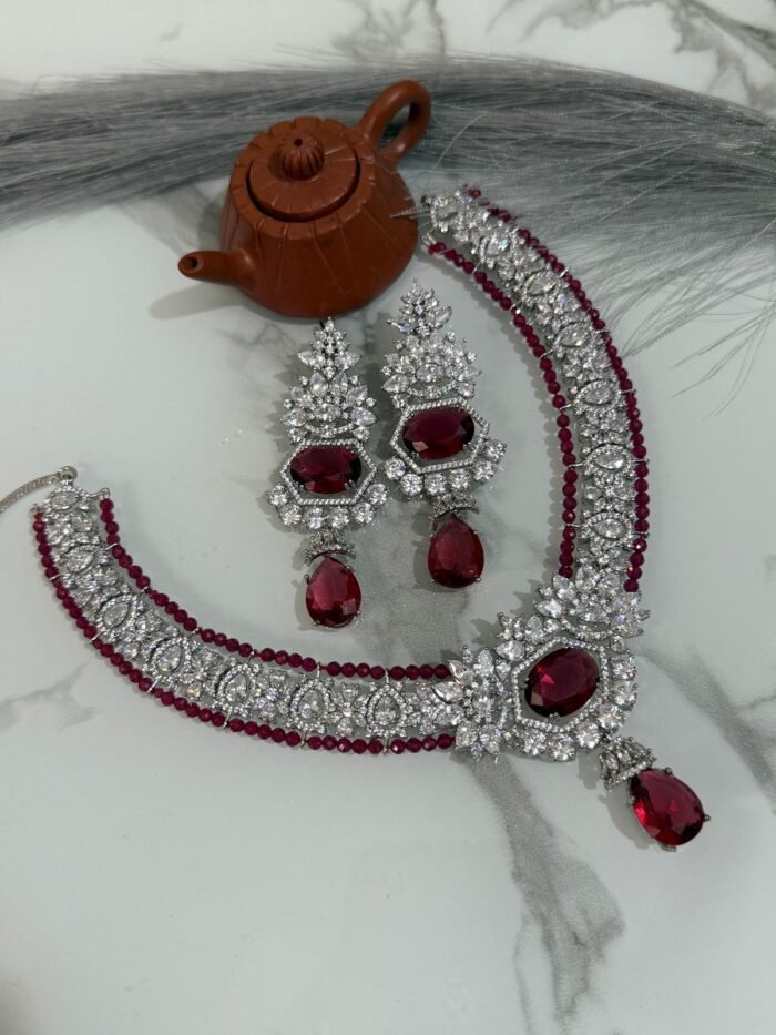 Ruby and diamond necklace set with matching earrings displayed on a marble surface, featuring a rich ruby strand and sparkling diamonds.
