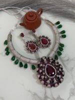 Ruby and diamond necklace set with green bead accents and matching earrings displayed on a marble surface.