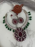Ruby and diamond necklace set with green bead accents and matching earrings displayed on a marble surface.