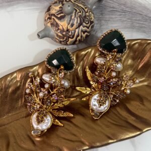 Gold-plated earrings with green stones, pearls, and floral design displayed on a golden leaf tray with decorative teapots in the background.