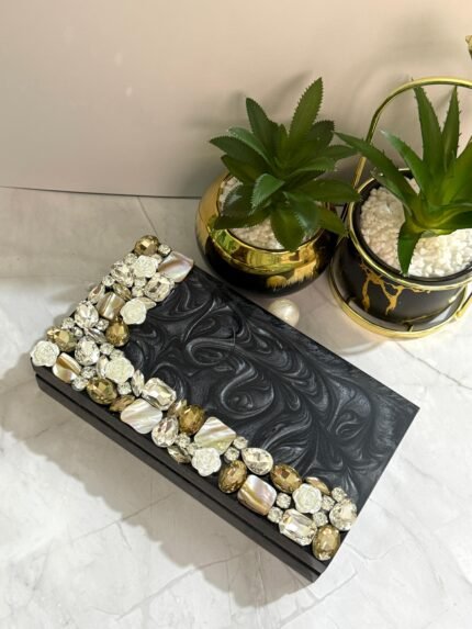 A stylish black clutch with sparkling crystal and mother-of-pearl embellishments, perfect for adding elegance to formal occasions and special events.