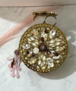 A gold clutch with crystal embellishments, featuring a floral design and pink bead tassel, placed on a marble surface.