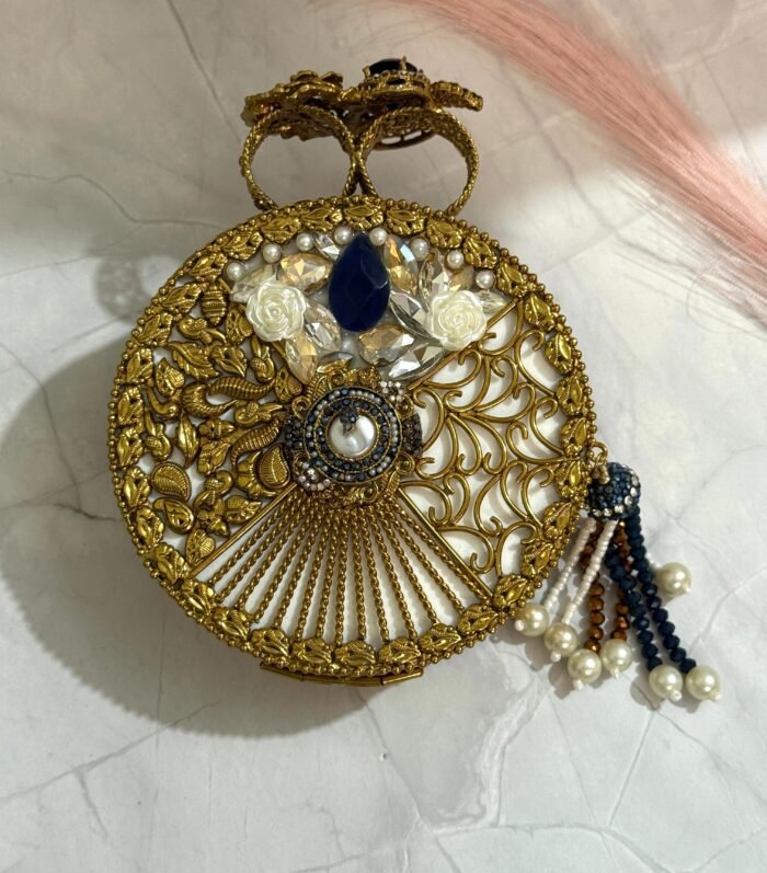 A turquoise and gold clutch adorned with sparkling crystals and a pearl tassel, placed on a marble surface.