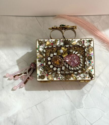A multi-colored crystal and gold embellished clutch with a pink bead tassel, featuring intricate detailing, placed on a marble surface.
