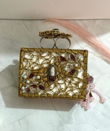 A multi-colored crystal and gold embellished clutch with a pink bead tassel, featuring intricate detailing, placed on a marble surface.