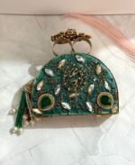 A green clutch with gold accents, sparkling crystals, green gemstones, and pearl tassels, placed on a marble surface.