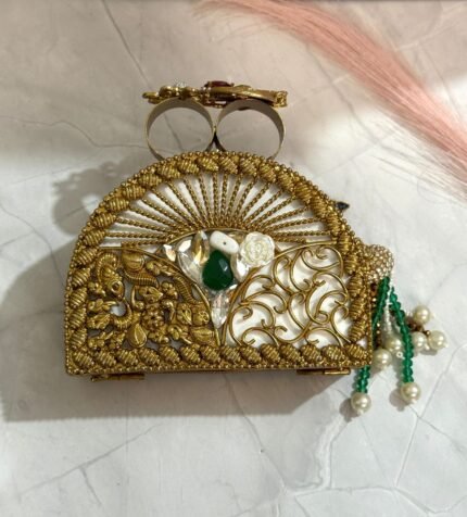 A green clutch with gold accents, sparkling crystals, green gemstones, and pearl tassels, placed on a marble surface.