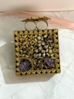A gold floral and crystal embellished clutch with lavender gemstones, featuring intricate detailing, placed on a marble surface.