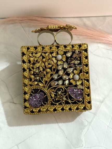 A gold floral and crystal embellished clutch with lavender gemstones, featuring intricate detailing, placed on a marble surface.