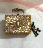 A pink and gold embellished clutch with crystal and gemstone detailing, featuring a beaded tassel, placed on a marble surface.